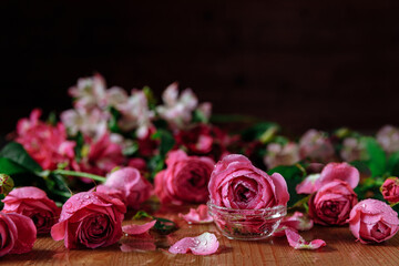 Fresh pink roses flowers with petals an leaves on the wooden table and dark black background. Still life. Copy space