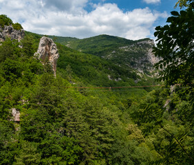 Obraz premium A climber at a high altitude above the mountain slopes overgrown with forest. Constructs a cableway over the great Crimean canyon. Crimea.