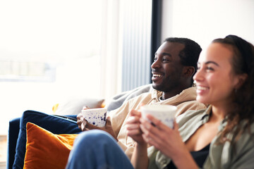 Smiling Young Couple Relaxing At Home Sitting On Sofa Watching On Demand TV Together
