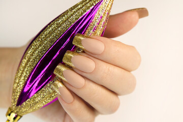 Golden fashion French manicure on long nails with sequins and Christmas toys.