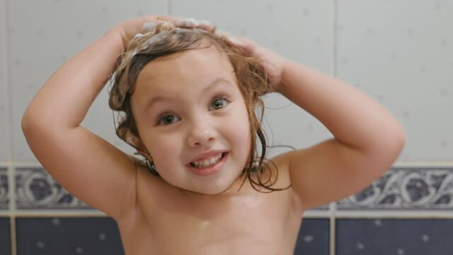 Portrait of little girl washes shampoo her hair and smiles in the bath at home