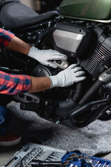 Fototapeta na wymiar cropped view of repairman in gloves checking motorbike near toolbox in workshop