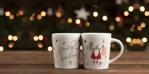 Cups on a wooden table against the background of a Christmas tree. Merry Christmas and Happy New Year