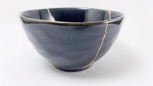 Gold cracks Kintsugi, broken black repaired cup, Kintsukuroi Japanese technique.