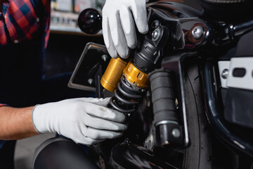 cropped view of mechanic checking shock absorber of motorcycle in workshop - obrazy, fototapety, plakaty