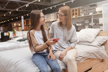Fototapeta premium Teenage girl and her mom talking while using smart phone together