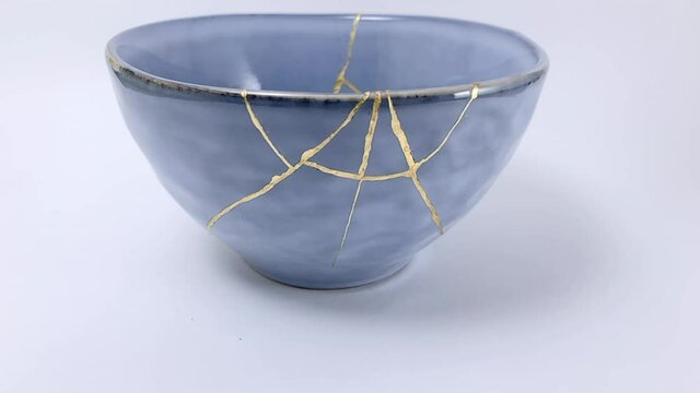 Kintsugi, slow motion video, broken blue and grey repaired cup, Kintsukuroi Japanese technique, gold scars restoration.