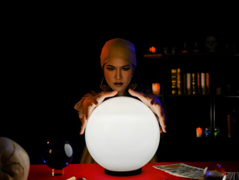 Asian woman fortune teller using magical occult divine power crystal call to forecast luck on red table. 