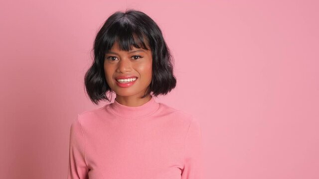 Cheerful dark skinned woman with wavy hair crosses fingers for good luck believes in her success dressed in casual poloneck isolated over pink background. Superstitious female prays for wellness