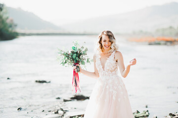 Fototapeta na wymiar Portrait of stunning bride with long hair posing with great bouquet near river