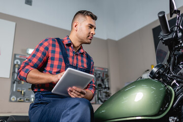 low angle view of mechanic using digital tablet while sitting on motorcycle in workshop