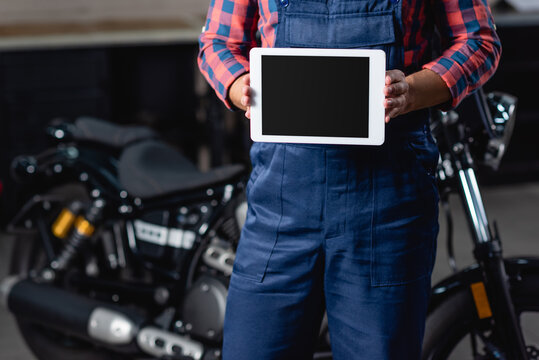 partial view of mechanic holding digital tablet with blank screen near motorbike on blurred background
