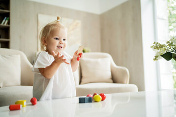 beautiful baby girl playing at home alone with her children's colored toys for development. on the table in the living room. Blonde of European appearance