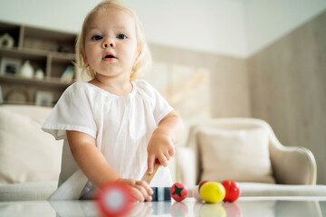 baby girl playing at home alone with her children's games on the table in the living room. Blonde of European appearance