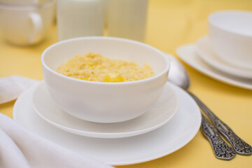 Millet porridge with butter in a white ceramic cup on a yellow tablecloth. Healthy eating. Healthy breakfast.