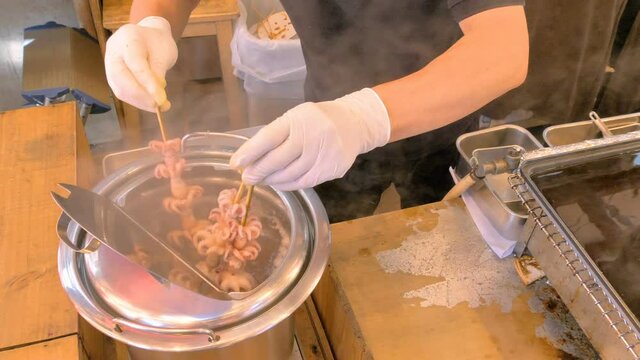 The man dipping the food in stick in the hot water in Tokyo Japan inside the restaurant in Tsukiji fish market