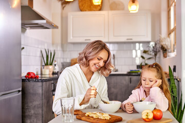 child girl doesn't want eat breakfast, sit behind table want to sleep, in light modern kitchen in the morning
