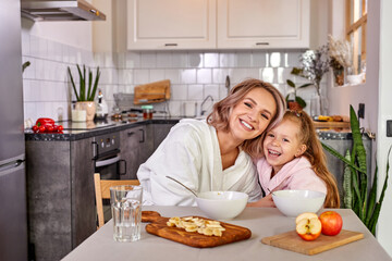mother and child girl have fun in the kitchen while having meal, breakfast together. smile, laugh, talk, friendly mother and daughter in the morning