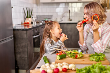 cute mom and child girl tasting fresh fruits while preparing salad for dinner, carving it together, have fun, smile. food, meal concept