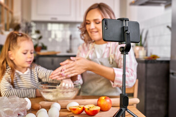 food blogger mother and daughter preparing the dough, bake cookies, record video on camera, enjoy. in the kitchen. focus on mobile phone on a tripod