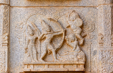 Hampi, Karnataka, India - November 4, 2013: Hazara Rama Temple. Closeup of beige stone damaged sculpture on wall featuring battle scene with bow, arrow, shield and clubs.
