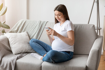 Pregnancy Tracker App. Smiling Young Pregnant Lady Using Smartphone At Home