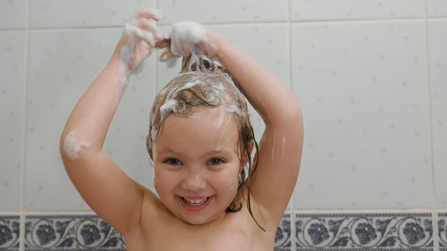 Cute little girl shampoos her hair and makes funny hairdo in the bath at home