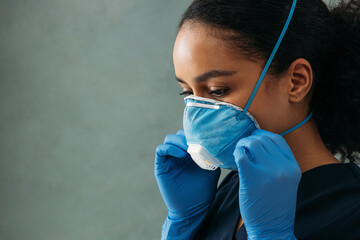 
Close up of young nurse adjusting respirator on her face
