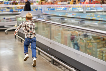 child boy running in the aisle of grocery store, having fun during shopping