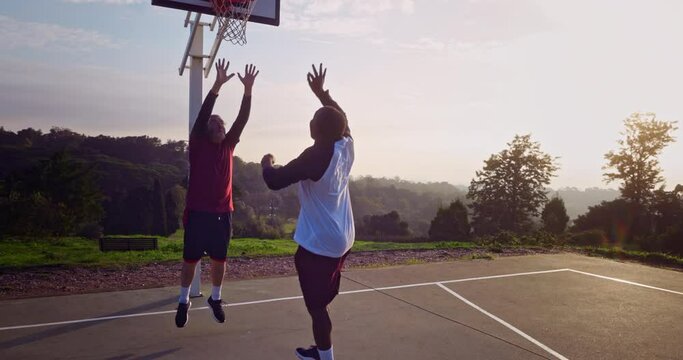 Two senior men playing basketball on outdoors court at sunrise