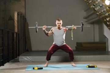 Physically strong disabled armless man training in the gym. Tackling barbell weight, doing back squat exercise, holding left side with forearm stump.