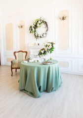 Fototapeta na wymiar Luxury stylish bright light interior of sitting room. White walls decorated by ornament. Fireplace. Nobody inside room. Table setting by dishes, candles and flower bouquets.