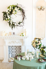 Luxury stylish bright light interior of sitting room. White walls decorated by ornament. Fireplace. Nobody inside room. Table setting by dishes, candles and flower bouquets.