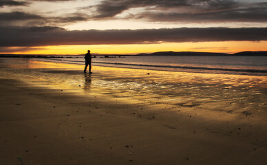 Fototapeta na wymiar Beautiful morning orange sunrise with silhouetted man walking down the Silverstrand beach in Galway, Ireland 