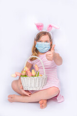 Coronavirus and Easter holiday. Cute little girl in a protective medical mask with bunny ears. Easter banner background. with Easter eggs and spring flower in basket
