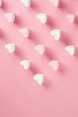 Heart shaped marshmallows are placed in rows on a pink background with space to write your text.
