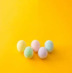 Colorful stacked up easter eggs on a bright yellow gold background. Creative minimal spring art.