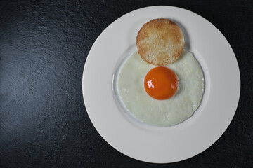 Breakfast of eggs on a white plate and black stone. Top view with copy space