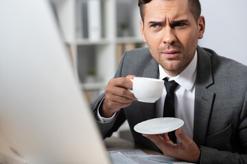 thoughtful businessman holding coffee cup at workplace, blurred foreground