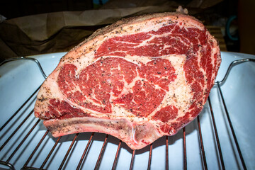 Two bone standing rib beef roast raw with salt and pepper rubbed on sitting on rack in roasting pan