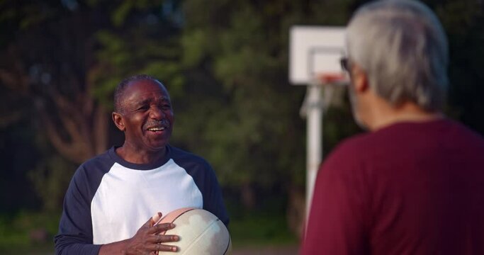 Senior african-american man laughing with friend holding basketball on outdoors