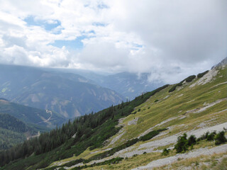 Fototapeta premium A panoramic view on the Austrian Alps from the Hochkogel peak. Thick clouds above the region. Endless mountain chains. The slopes are overgrown with small plants and trees. Mysterious landscape.