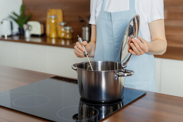 Woman standing on modern kitchen, cooking food in saucepan