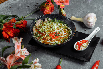Asian cuisine, Beef soup fo in a black plate on a dark background. Soup Fo with Spicy beef broth, beef tenderloin, udon noodles, chili paste