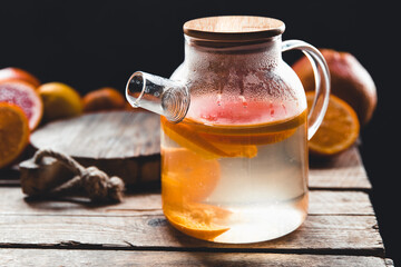 Citrus tea in a transparent teapot and a glass, healthy drink on a wooden background.