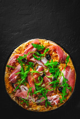 Pizza with Mozzarella cheese, ham, pepper, olive, meat, Tomato sauce, Spices and Fresh arugula. Italian pizza on black plate on Dark grey black slate background