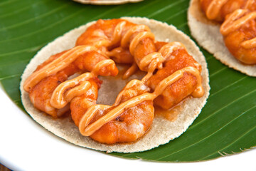 Mexican chipotle shrimp tacos, served on a white square plate with banana leaf on wooden background, close up view