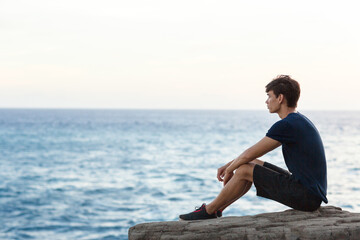 Naklejka na ściany i meble Young man sitting alone watching the ocean view.