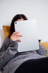 Unrecognizable woman using a silver digital tablet and lying on a bed
