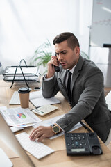 serious businessman talking on telephone while typing on computer keyboard, blurred foreground